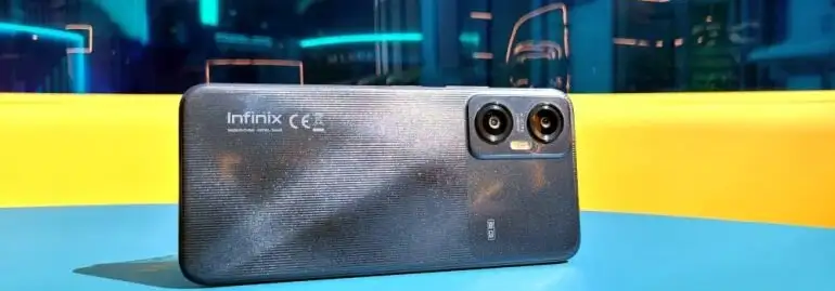 Szary telefon Infinix leży na niebieskim stole. W tle żółta i niebieska ściana. Widoczne dwa obiektywy aparatu.