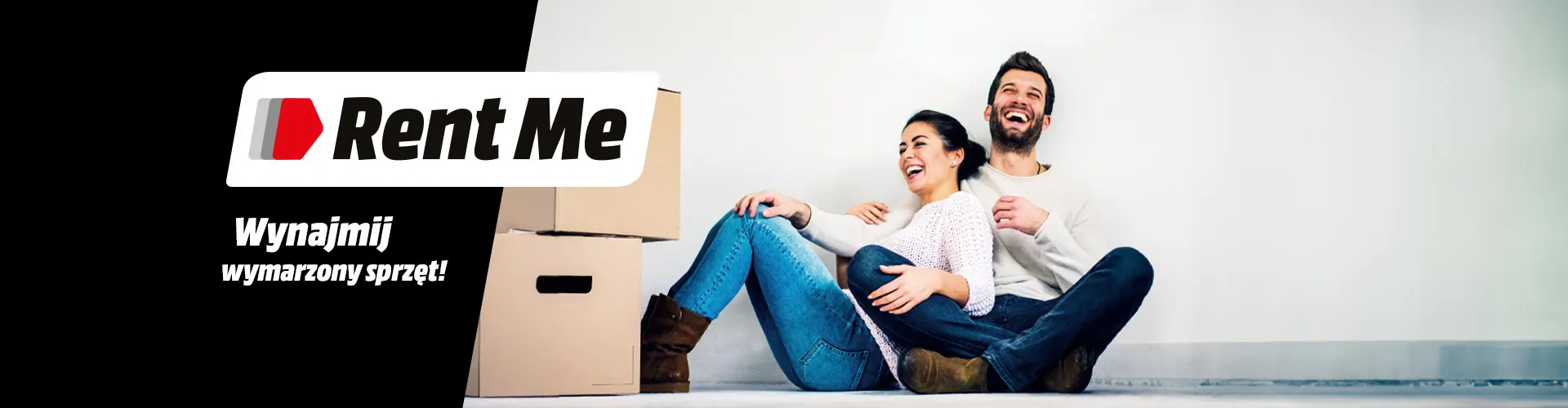 Para siedzi na podłodze obok kartonów, logo „Rent Me” na czarnym tle, napis „Wynajmij wymarzony sprzęt!”.