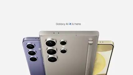 Trzy telefony: fioletowy z trzema obiektywami, szary z pięcioma i złoty. U góry napis "Galaxy AI is here" na białym tle.