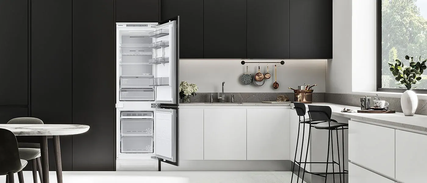 Nowoczesna kuchnia z czarnymi szafkami i białymi blatami. Otwarta biała lodówka, stół z krzesłami, okno. Naczynia wiszą na relingu.