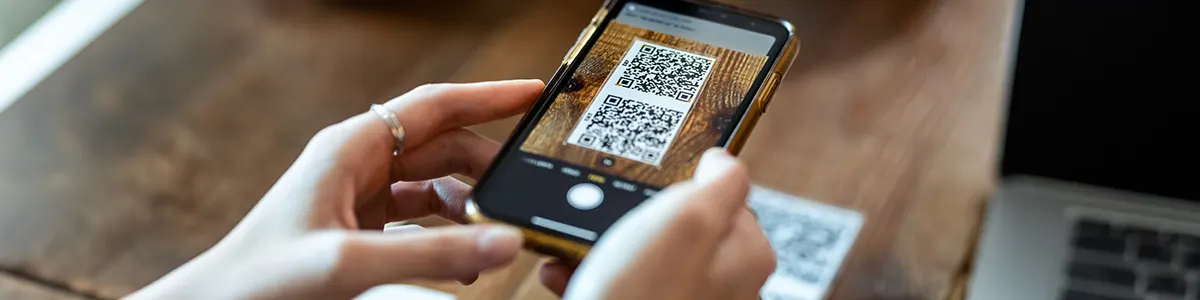 Kobieta skanująca telefonem kod QR leżący na blacie stołu. 