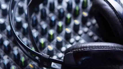 Słuchawki na mikserze dźwięku z wieloma pokrętłami i suwakami, tworzące skomplikowany panel kontrolny w studiu nagraniowym.