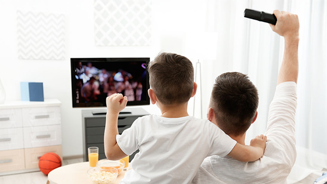 Ojciec z synem na kanapie przed małym telewizorem w jasnym salonie.