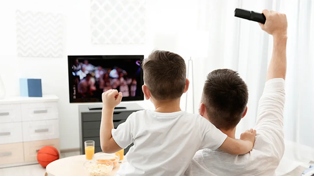 Ojciec z synem na kanapie przed małym telewizorem w jasnym salonie.