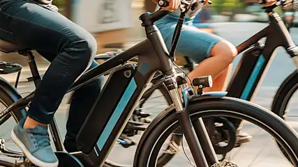 Dwie osoby jadą na rowerach elektrycznych po ulicy miasta w słoneczny dzień.