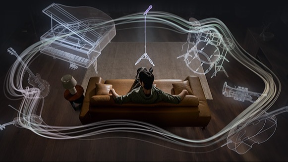 Osoba w słuchawkach siedzi na kanapie w ciemnym pokoju; wokół świetlne fale i półprzezroczyste kontury instrumentów (fortepian, mikrofon, perkusja, trąbka, skrzypce, wiolonczela) — efekt immersyjnego, przestrzennego dźwięku.