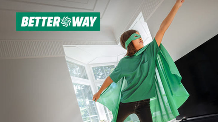 Chłopiec w masce i pelerynie stoi w pokoju z podniesioną ręką. W tle okno i logo firmy Better Way.