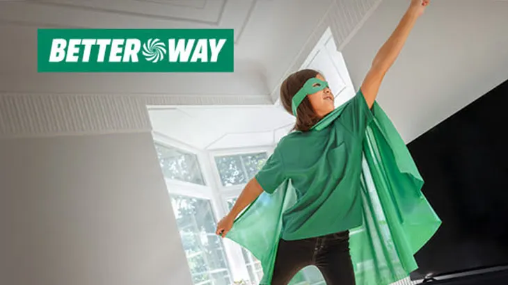 Chłopiec w masce i pelerynie stoi w pokoju z podniesioną ręką. W tle okno i logo firmy Better Way.