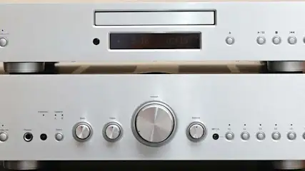 Dwa srebrne urządzenia audio ustawione jedno na drugim, z przyciskami i pokrętłami na jasnym tle.