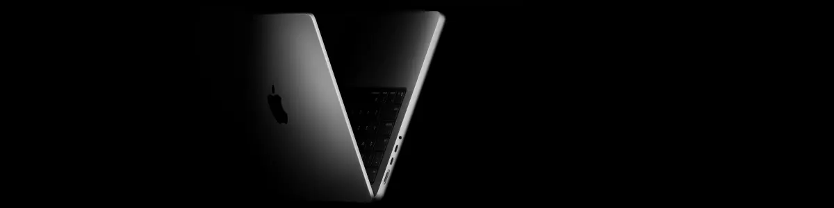 Nowy Apple MacBook Pro 14 cali (2025) z M5 położony "na plecach", na łączeniu ekranu z klawiaturą, rozłożony 45 stopni, czarne tło. 