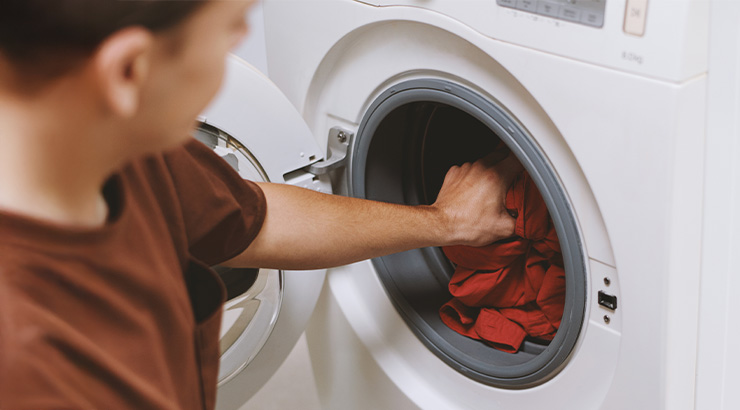 Osoba wkłada czerwone ubrania do białej pralki z otwartymi drzwiami.