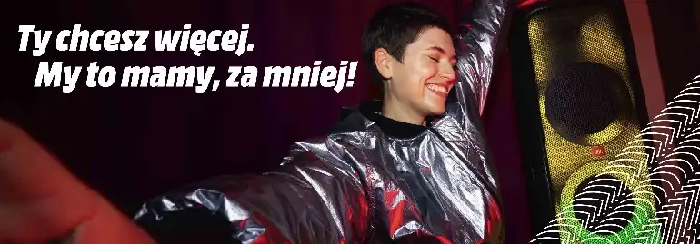 Uśmiechnięta osoba w srebrnej kurtce stoi obok głośnika. Obok widnieje tekst: "Ty chcesz więcej. My to mamy, za mniej!".
