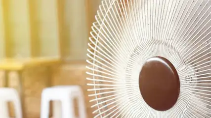 Na pierwszym planie biały wentylator z brązowym środkiem, w tle stolik i białe krzesła.