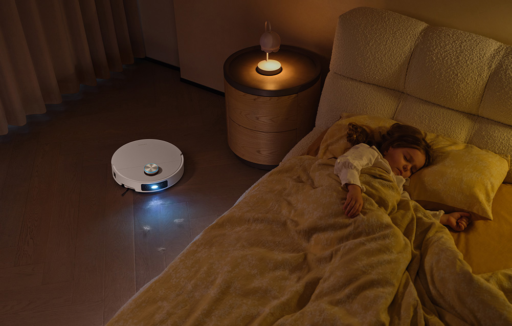 Na grafice widać sprzątający robot Dreame w pokoju dziecięcym, w którym śpi mała dziewczynka.