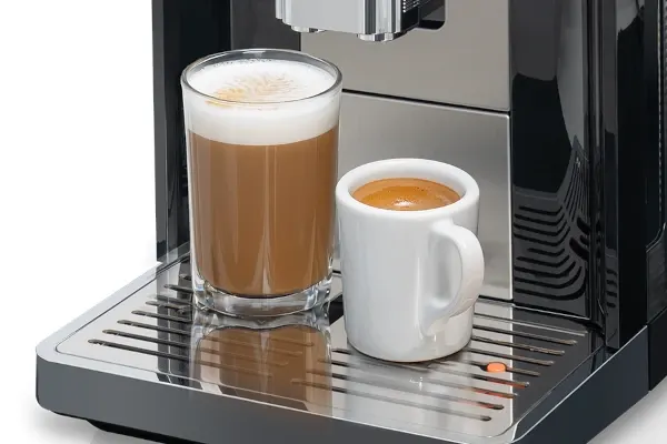 Automatyczny ekspres do kawy KOENIC Cremaro+ z wysoką kawą mleczną i filiżanką espresso na metalowym ociekaczu.