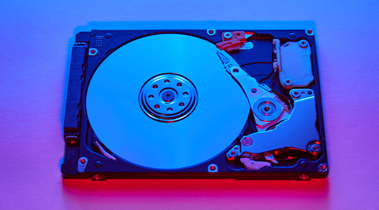 Otwarty dysk twardy z talerzem i głowicą na fioletowo-niebieskim tle, ukazujący jego wewnętrzną konstrukcję.