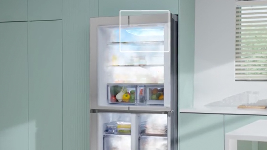 Otwarta lodówka w miętowej kuchni; białe obramowanie podświetla górną półkę z niebieską poświatą – wizualizacja cyrkulacji chłodnego powietrza. Na półkach i w szufladach widoczne warzywa i produkty; na dole szuflady zamrażarki.