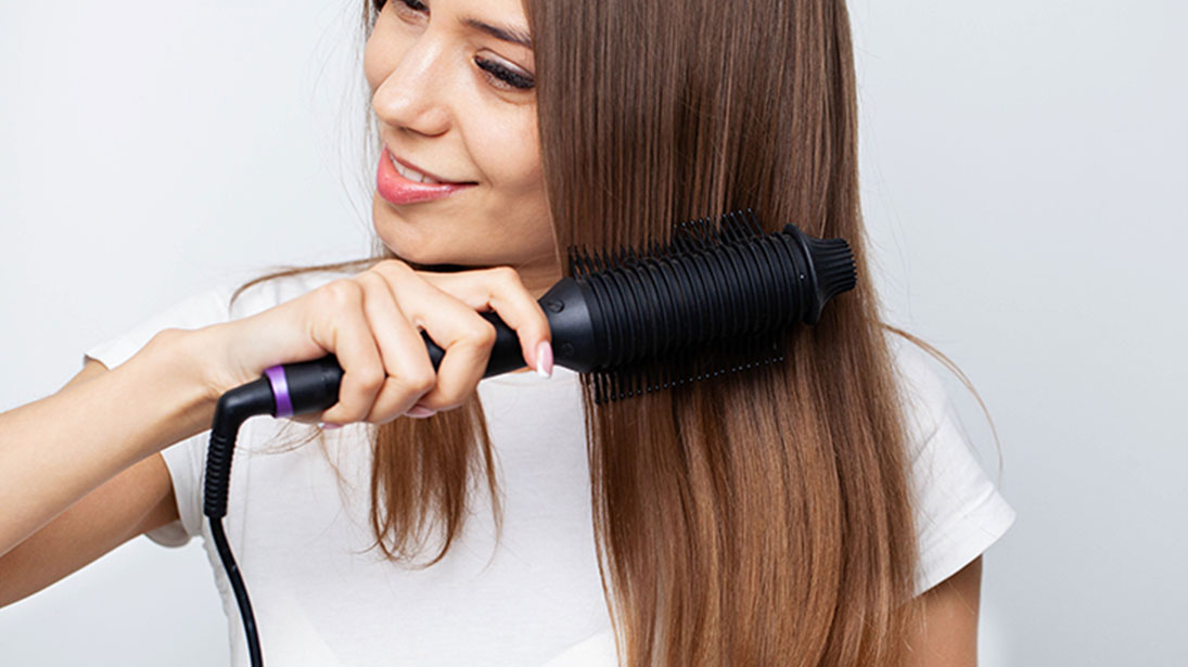 Kobieta w białej koszulce używa czarnej prostującej szczotki do włosów na białym tle.