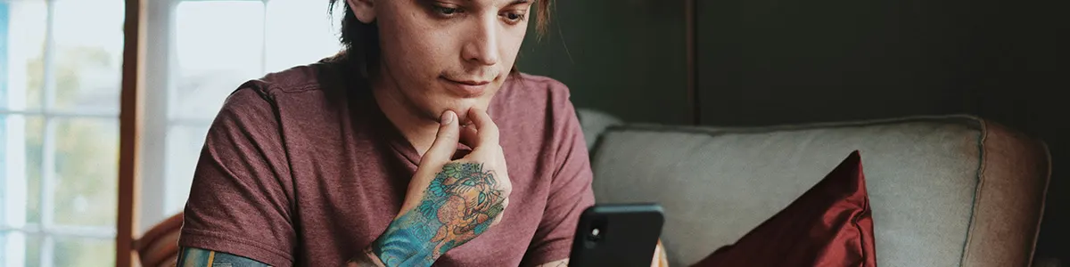 Mężczyzna z tatuażem na dłoni sprawdzający numer telefonu na swoim smartfonie.