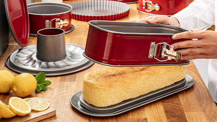 Na stole blacha z ciastem, forma do pieczenia, cytryny, deska do krojenia i ręce trzymające formę.