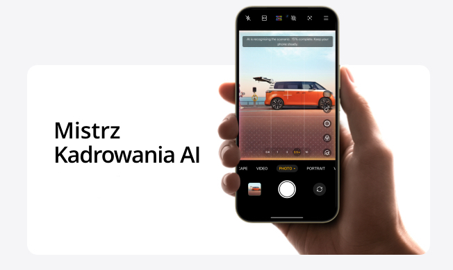 Dłoń trzymająca smartfon, na ekranie którego widnieje interfejs aparatu z pomarańczowym kamperem w kadrze. Nad obrazem kampera widoczny jest komunikat 'AI is recognizing the scene. 15% complete. Keep your phone steady.' Po lewej stronie ekranu, na ciemniejszym tle, widnieje napis 'Mistrz Kadrowania AI'.