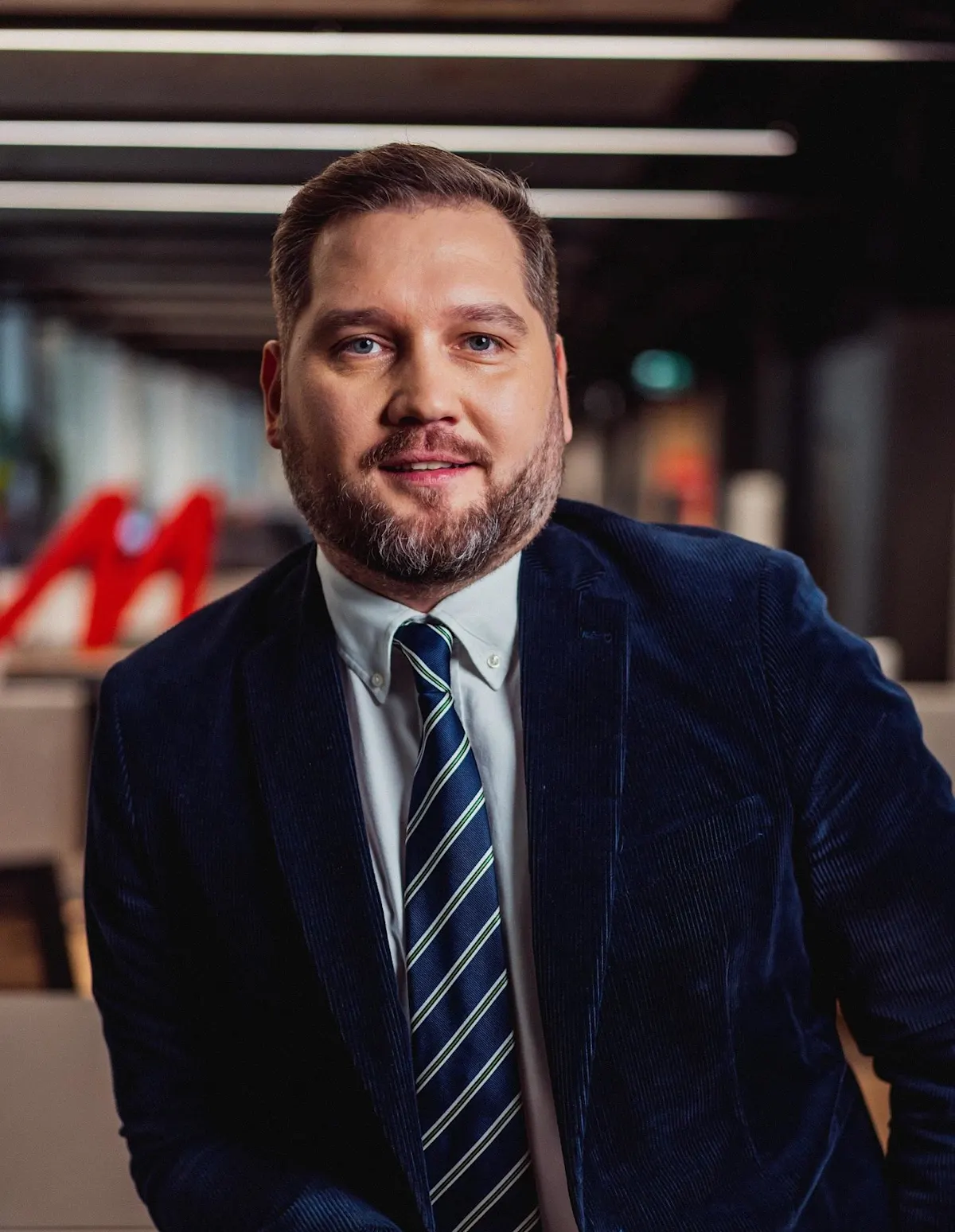Marcin Walendowski w granatowej marynarce i krawacie w paski stoi na tle biura.