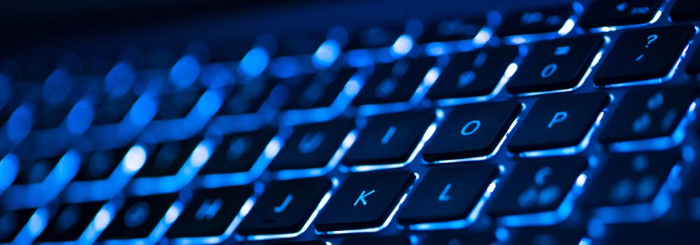 Czarno-niebieska klawiatura podświetlana od spodu. Widoczne litery J, K, L, O, P oraz cyfra 0 i znak zapytania.