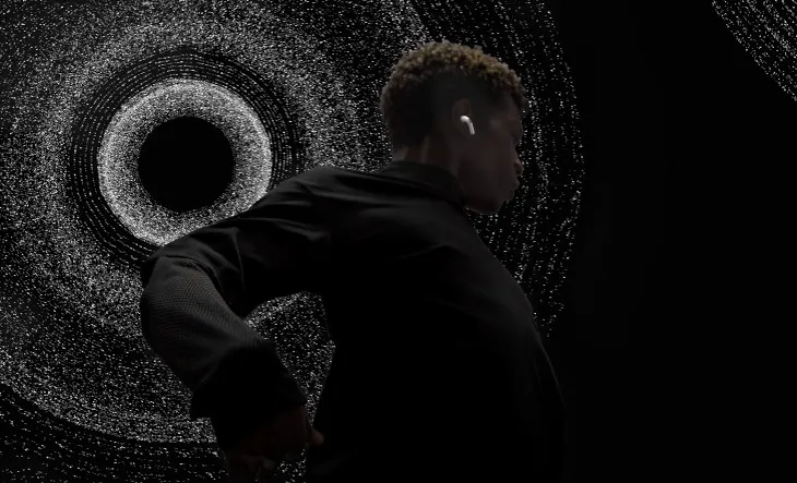 Osoba w słuchawce stoi na tle grafiki imitującej czarną dziurę, na czarnym tle.