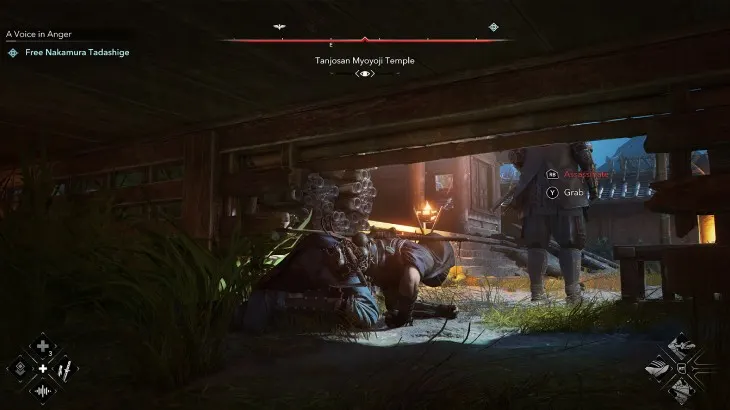 Mężczyzna w ciemnym stroju leży na ziemi pod drewnianą konstrukcją, w tle stoi postać. Świeci się ogień.