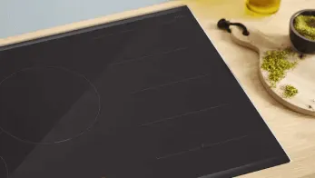 Czarny blat kuchenny obok deski do krojenia z ziołami i miseczki, na drewnianym blacie. W tle butelka z płynem.