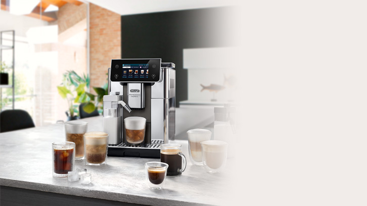 Na blacie kuchennym stoi ekspres do kawy obok szklanek z różnymi kawami. W tle widać okno i elementy wystroju wnętrza.