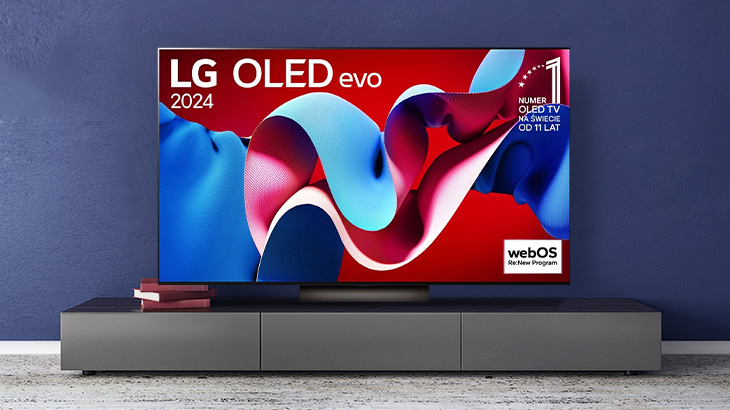 Telewizor LG OLED na szafce RTV, na ekranie grafika z logo LG i webOS, ściana w kolorze ciemnoniebieskim.