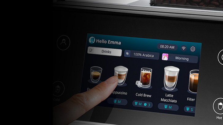 Ekran ekspresu do kawy z wyborem napojów: Espresso, Cappuccino, Cold Brew, Latte Macchiato i Filtr. Palec dotyka ikony Cappuccino.