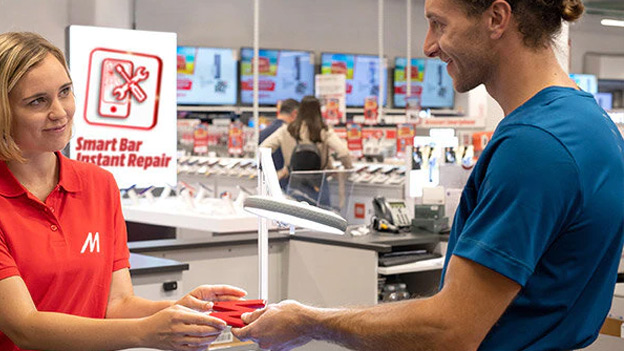 Kobieta w czerwonej koszulce podaje czerwone etui mężczyźnie w niebieskiej koszulce przy ladzie "Smart Bar Instant Repair" w sklepie.