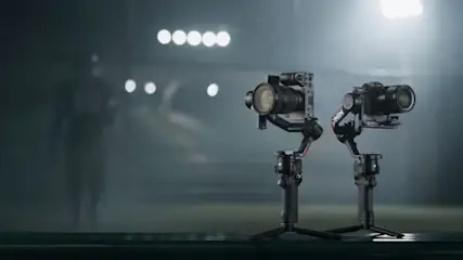 Dwa czarne aparaty fotograficzne stojące na statywach na ciemnym tle z rozmytymi światłami.