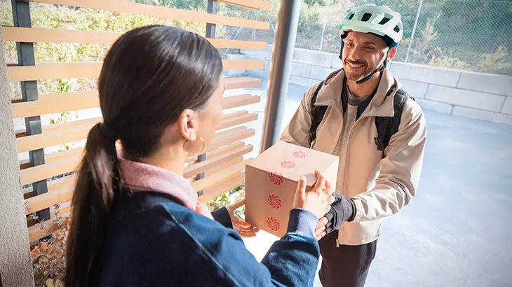 Kobieta odbierająca paczkę od kuriera z kaskiem rowerowym na głowie