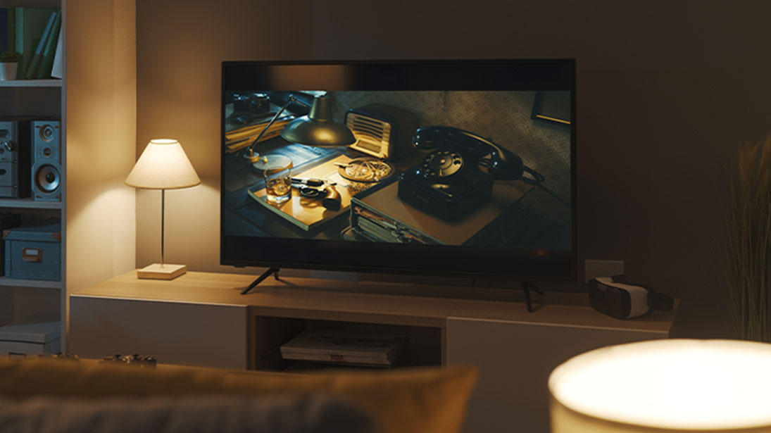 Znakomity kontrast w ciemnej scenie na telewizorze OLED 65 cali. Na ekranie stary biurko ze starymi telefonem i radiem.