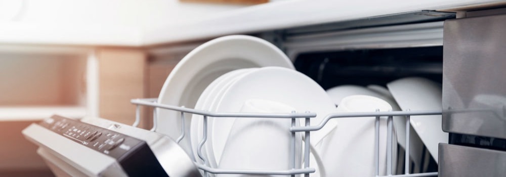 Otwarta zmywarka z metalowym koszem wypełnionym białymi talerzami. Widoczne przyciski na obudowie zmywarki.