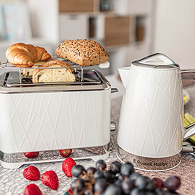 Na stole toster z pieczywem, czajnik, truskawki i winogrona. W tle szafki kuchenne.