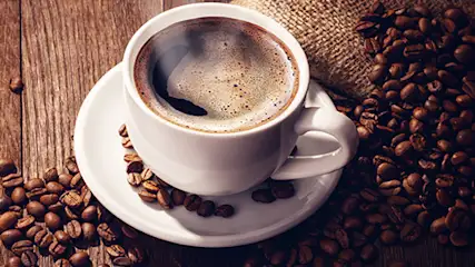 Filiżanka aromatycznego napoju stojąca na stole w otoczeniu ziaren kawy.