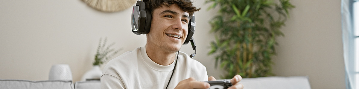 Mężczyzna z aparatem na zębach i słuchawkami na uszach trzyma pada w ręku. 