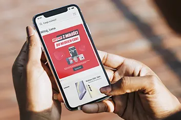 Osoba trzyma smartfon z ekranem wyświetlającym ofertę promocyjną z czerwonym tłem i grafiką prezentującą elektronikę.