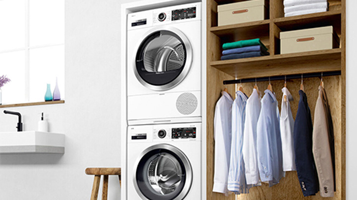 Pralka i suszarka stojące obok wyprasowanych ubrań