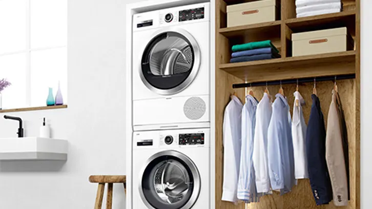 Pralka i suszarka stojące obok wyprasowanych ubrań