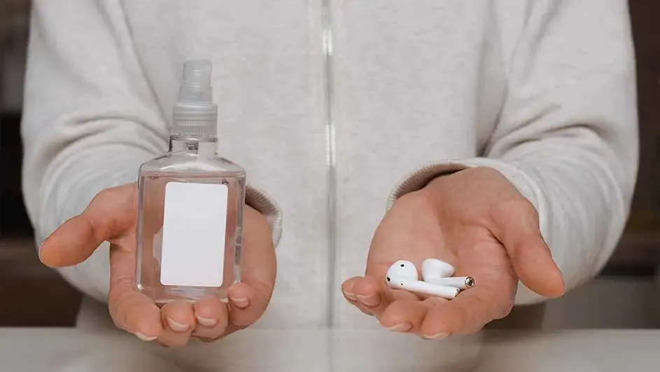 Osoba trzyma w dłoniach płyn do dezynfekcji w przezroczystej butelce i białe słuchawki bezprzewodowe.
