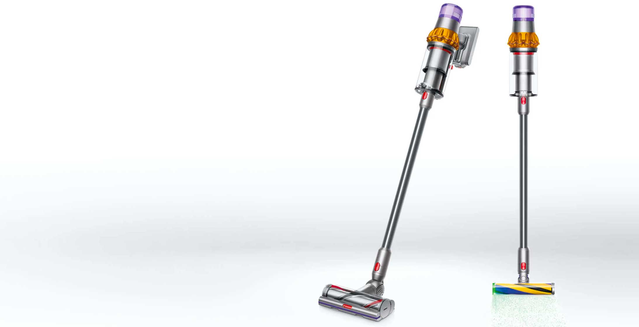 Dwa odkurzacze pionowe na białym tle. Jeden odkurzacz jest pochylony, drugi stoi prosto. Odkurzacze są srebrne, z żółtymi i fioletowymi akcentami.