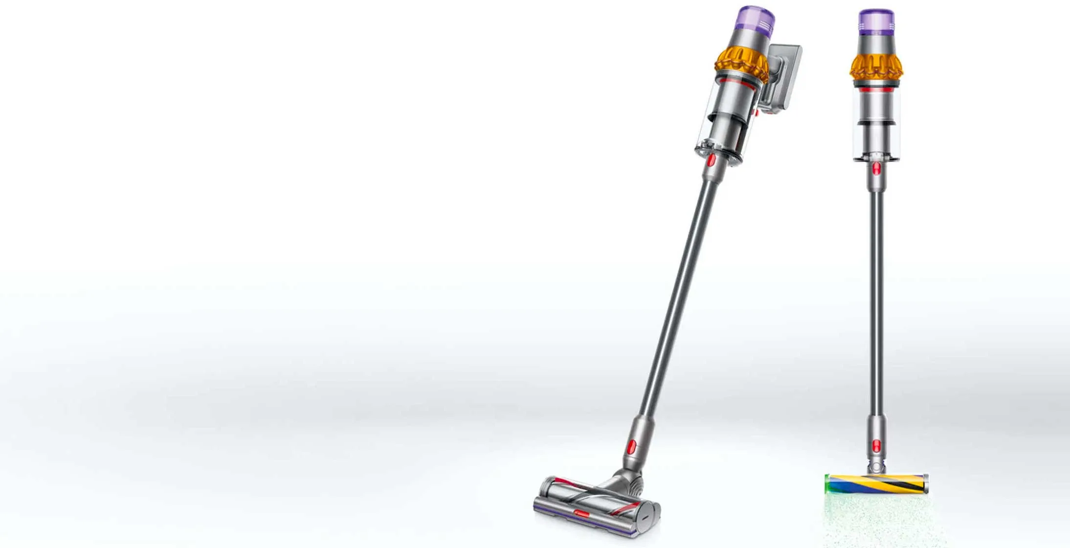 Dwa odkurzacze pionowe na białym tle. Jeden odkurzacz jest pochylony, drugi stoi prosto. Odkurzacze są srebrne, z żółtymi i fioletowymi akcentami.