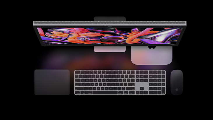 Widok z góry na biurko z komputerem, klawiaturą, myszą i touchpadem na czarnym tle. Ekran monitora wyświetla abstrakcyjną grafikę.