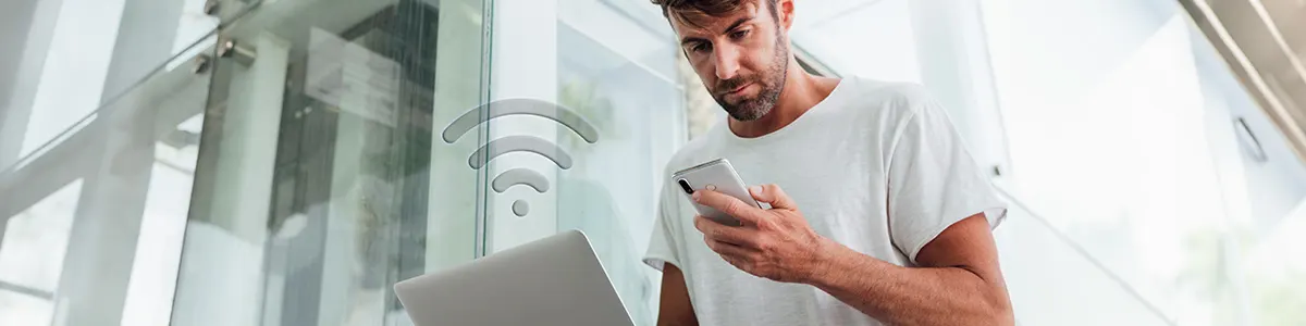 Stojący mężczyzna ze smartfonem w dłoni udostępnia internet z telefonu na swój laptop. 