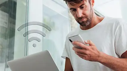 Stojący mężczyzna ze smartfonem w dłoni udostępnia internet z telefonu na swój laptop.